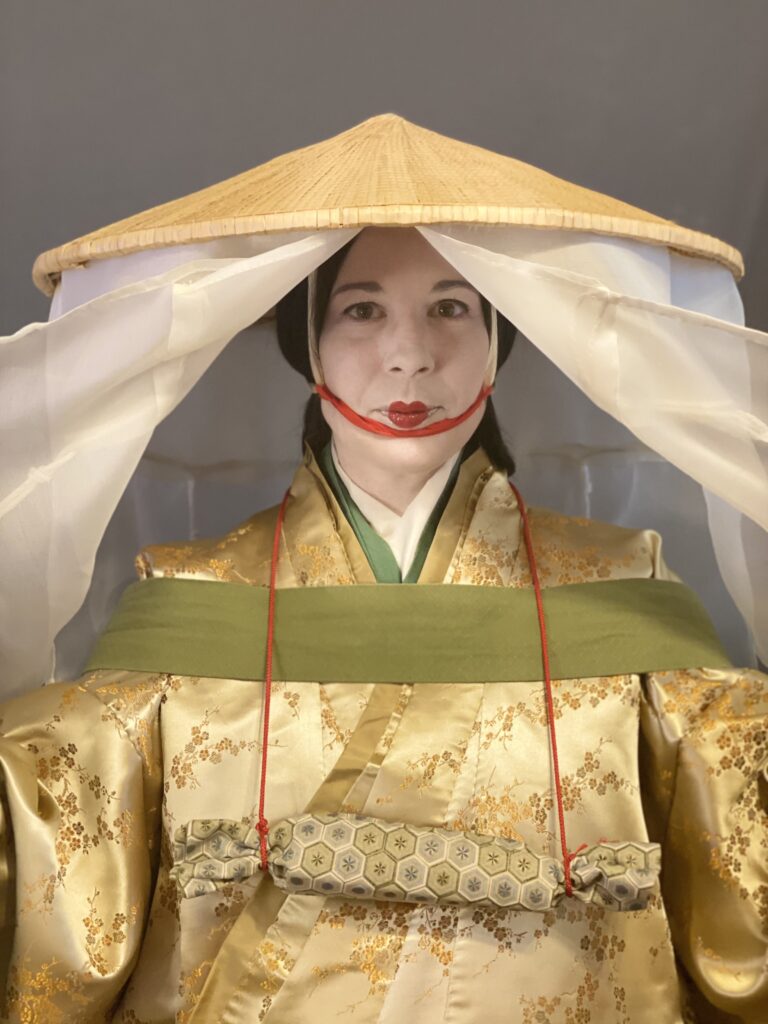 A woman wearing a Heian travelling outfit, the veil panels on the large hat spread wide to reveal her face and clothing.