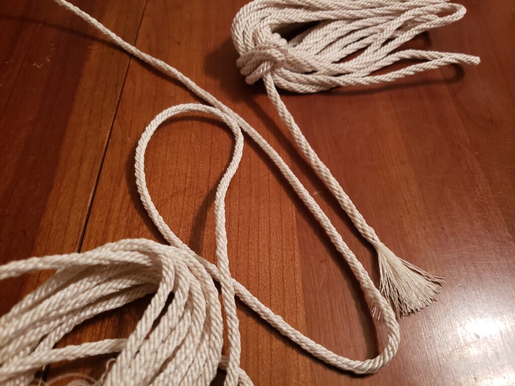 Two bundles of white braided cord sit opposite each other bottom left and top right. A segment extends from each bundle creating a diagonal from left to right. The cord on the left is slightly smaller and of finer texture than the cord on the right.