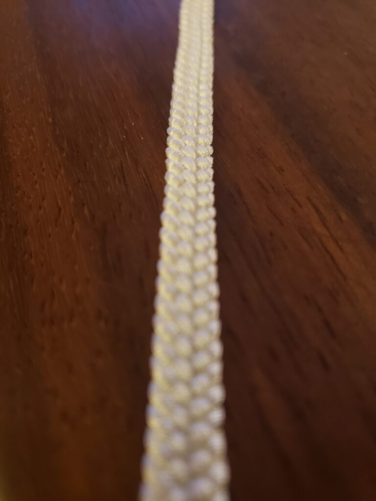 A white braided cord runs top to bottom, bisecting the image. The cord is an 8 strand flat braid.