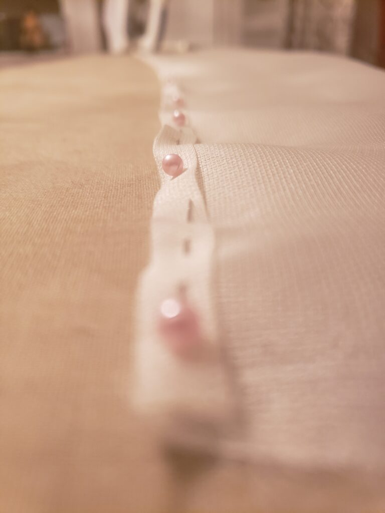 A piece of sheer silk in white extends away from the camera. The edge has been rolled twice, pressed and pinned along the length.