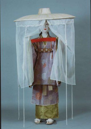The Costume Museum mannequin of a lady wearing a travelling outfit and ichime gasa with mushi no tareginu or hemp veiled sedge hat. The mannequin stands with her hands outstretched parting the sheer curtains hanging down from the very wide brimmed straw hat.