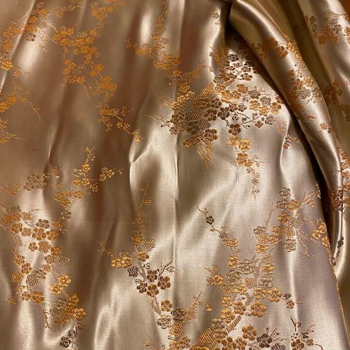 A light gold brocade fabric with dark gold and brown flower blossoms on branches