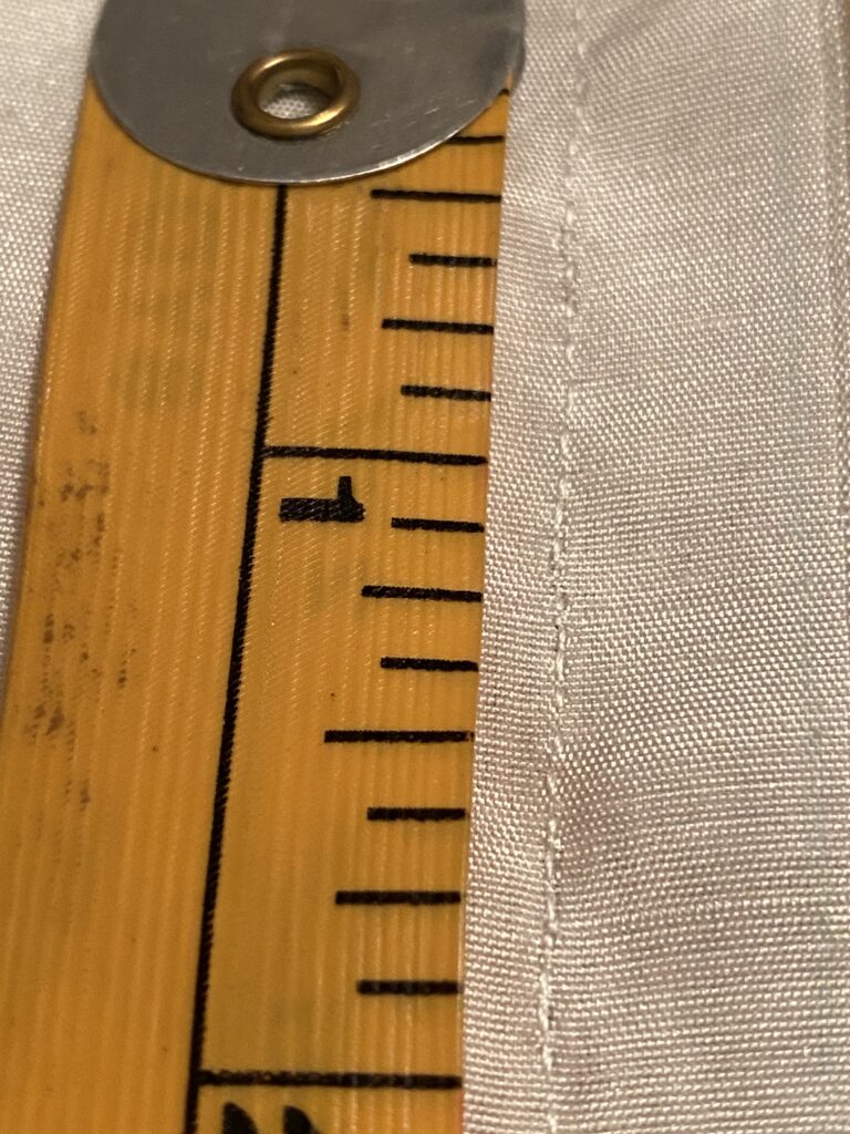 The first two inches of a yellow measuring tape next to a handsewn seam of approximately 20 stitches per inch.