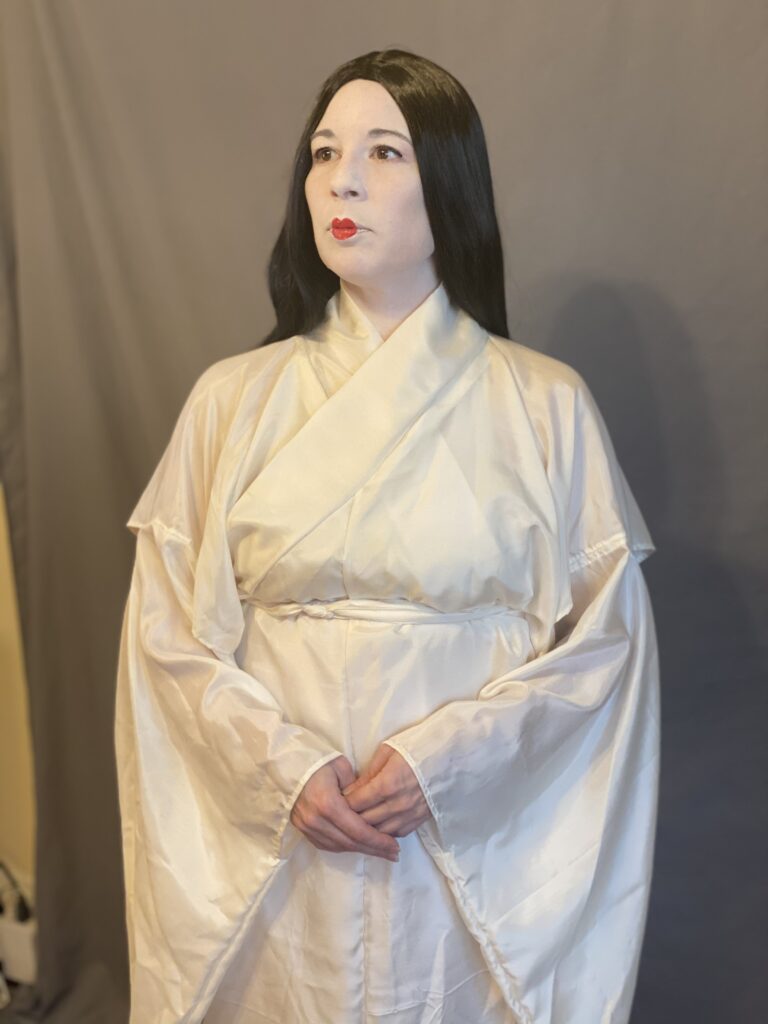 A woman with Heian make up (white face and small red lips) wearing a white silk kosode.