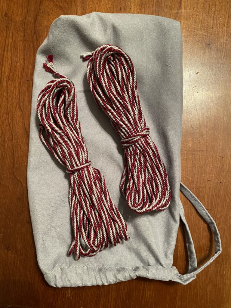 Two bundles of maroon and light grey cord, tied around the middle, sitting on a small light grey drawstring bag